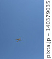 Distant Airplane Tiny Silhouette Against Large Expanse of Clear Blue Sky 140379035