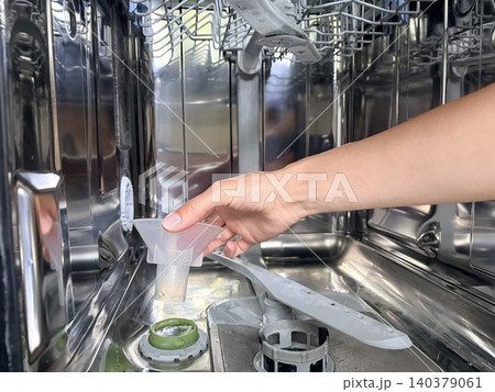 A photo of a woman's hand inserting a funnel inside a dishwasher to refill the salt supply. 140379061