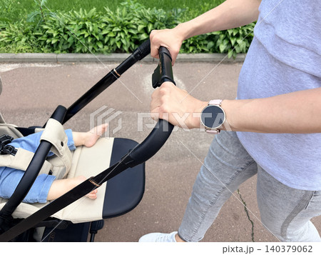 a mother pushing a baby stroller along a paved walkway. The baby's bare feet and legs are visible 140379062