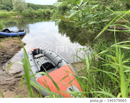 a serene river scene featuring two inflatable boats docked on a muddy, grassy bank. a peaceful and natural outdoor setting. 140379065