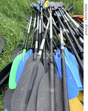 a large, disorganized pile of kayaking equipment resting on green grass. Active recreation on the river. Paddles for inflatable boats and kayaks. 140379066