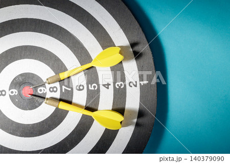 A top-down close-up view of a dartboard where two yellow flights darts have accurately pierced the red bullseye circle, signifying ultimate business success, accuracy, and goal achievement. A top-down close-up view of a dartboard where two yellow flights darts have accurately pierced the red bullseye circle, signifying ultimate business success, accuracy, and goal achievement. 140379090