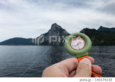 Hand holding a portable over Lake Traunsee with the Austrian Alps in the background, presenting a compact outdoor exploration tool 140379238