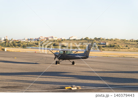 Small airplane parked on runway near city during evening light 140379443