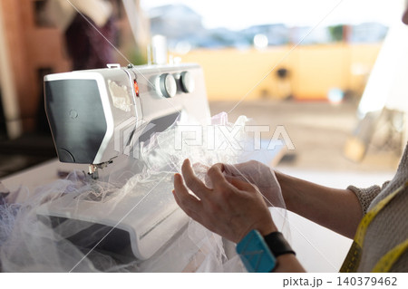 Sewing fabric with a sewing machine in a workspace during daylight hours 140379462