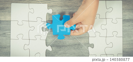 Hand of child putting together white and blue puzzle Hand of child putting together white and blue puzzle 140380877