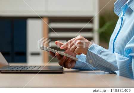 Side view close up hands of woman hold mobile phone over laptop and use the index finger to point or touch to screen of mobile phone in concept of modern business communication. 140381409