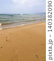 Waves softly lap against shore, creating serene ambiance on sandy beach. Footprints visible in golden sand, peaceful moment by water. Clear blue sea stretches out under light sky 140382090
