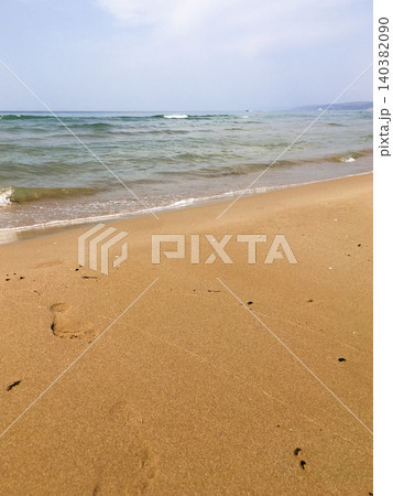 Waves softly lap against shore, creating serene ambiance on sandy beach. Footprints visible in golden sand, peaceful moment by water. Clear blue sea stretches out under light sky Waves softly lap against shore, creating serene ambiance on sandy beach. Footprints visible in golden sand, peaceful moment by water. Clear blue sea stretches out under light sky 140382090