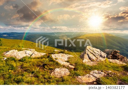 sunset over Carpathian mountain summer landscape. meadow with huge stones among the grass on top of the hillside near the peak of mountain range. alpine meadow and rolling hills. weather with rainbow sunset over Carpathian mountain summer landscape. meadow with huge stones among the grass on top of the hillside near the peak of mountain range. alpine meadow and rolling hills. weather with rainbow 140382177