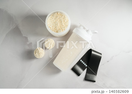 Protein shake, whey powder and resistance band on white background, fitness flat lay Protein shake, whey powder and resistance band on white background, fitness flat lay 140382609