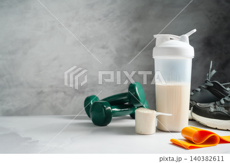 Protein shake and whey powder with dumbbells and running shoes, fitness nutrition concept, copy space Protein shake and whey powder with dumbbells and running shoes, fitness nutrition concept, copy space 140382611