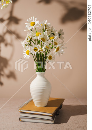 Daisy bouquet in ceramic vase with sunlight shadows, minimalist interior decor Daisy bouquet in ceramic vase with sunlight shadows, minimalist interior decor 140382702