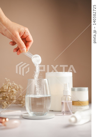 Collagen powder being added to pink beauty drink with skincare products and wellness concept 140382725