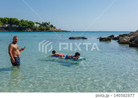 Father taking photo with a phone of two children swimming on a pool float in the sea Father taking photo with a phone of two children swimming on a pool float in the sea 140382877