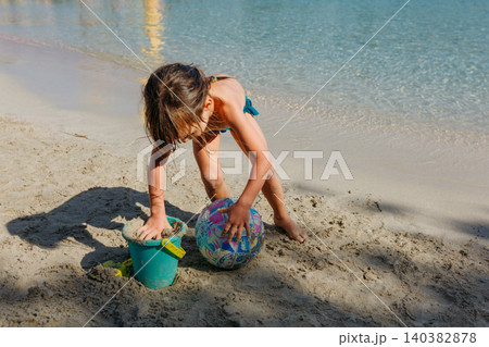 high angle view of a small child playing with sand on the beach high angle view of a small child playing with sand on the beach 140382878
