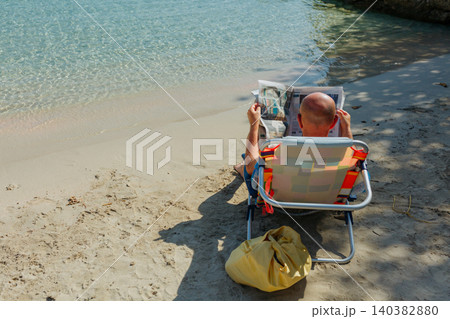 rear view of a Man Reading Newspaper in Beach Chair on Sunny Tropical Shore rear view of a Man Reading Newspaper in Beach Chair on Sunny Tropical Shore 140382880