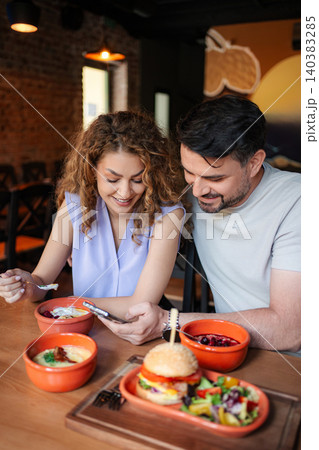 Happy couple looking at smartphone and eating in restaurant 140383285