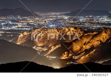 A panoramic night view from Mount Uhud overlooking the illuminated cityscape of Madinah with rugged mountain ridges in the foreground. A panoramic night view from Mount Uhud overlooking the illuminated cityscape of Madinah with rugged mountain ridges in the foreground. 140383327