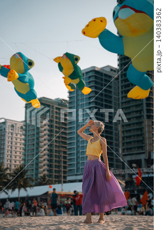 young woman walking on sand beach at colorful kite toys festival during summer sunset, girl enjoying freedom and joy at outdoor event by sea young woman walking on sand beach at colorful kite toys festival during summer sunset, girl enjoying freedom and joy at outdoor event by sea 140383362