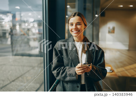 Happy young Caucasian woman in her twenties holding smartphone inside a cafe Happy young Caucasian woman in her twenties holding smartphone inside a cafe 140383946