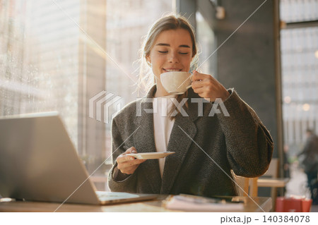 Happy young adult Caucasian woman drinking warm coffee at a modern cafe near window 140384078