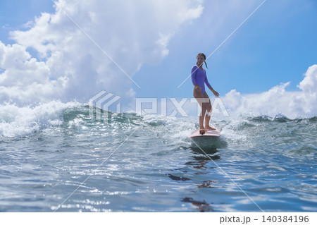 Cheerful Young Lady Balances On surfboard Amid Stormy Skies And Powerful Seas Cheerful Young Lady Balances On surfboard Amid Stormy Skies And Powerful Seas 140384196