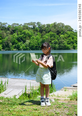 新緑の湖畔で立ち止まりしおりを読む遠足の女子小学生 140386348
