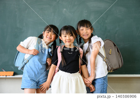 教室の黒板の前でカラフルなランドセルを背負い手をつなぐ笑顔の女子小学生たち 教室の黒板の前でカラフルなランドセルを背負い手をつなぐ笑顔の女子小学生たち 140386906