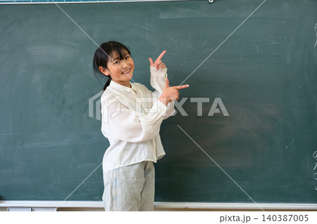 教室の黒板の前で笑顔で指差しをする高学年の女子小学生 140387005