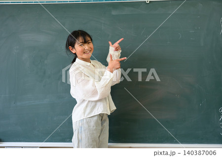 教室の黒板の前で笑顔で指差しをする高学年の女子小学生 教室の黒板の前で笑顔で指差しをする高学年の女子小学生 140387006