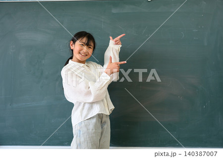 教室の黒板の前で笑顔で指差しをする高学年の女子小学生 教室の黒板の前で笑顔で指差しをする高学年の女子小学生 140387007