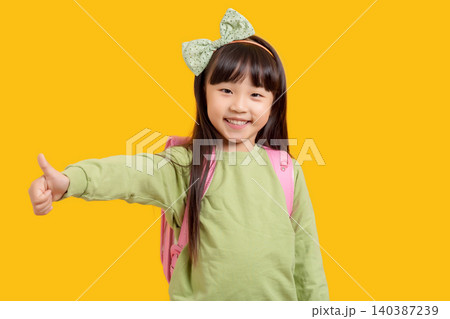 Happy Asian schoolgirl showing thumbs up, excited child with backpack on yellow background, approval and success concept Happy Asian schoolgirl showing thumbs up, excited child with backpack on yellow background, approval and success concept 140387239