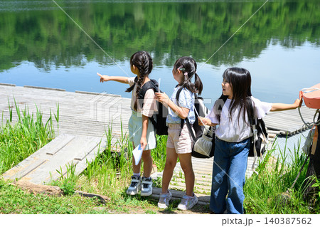 新緑の湖畔で地図を持ち驚いた表情で遠くを見上げる女子小学生たち 新緑の湖畔で地図を持ち驚いた表情で遠くを見上げる女子小学生たち 140387562