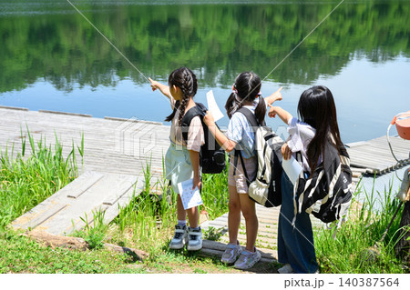 新緑の湖畔で地図を持ち驚いた表情で遠くを見上げる女子小学生たち 新緑の湖畔で地図を持ち驚いた表情で遠くを見上げる女子小学生たち 140387564