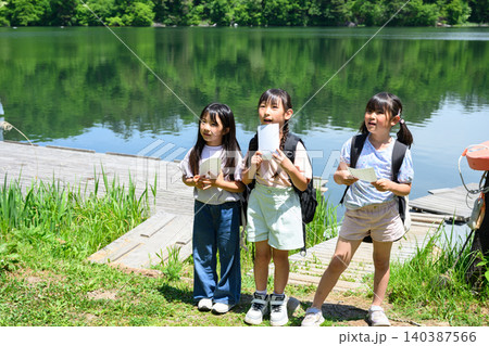 新緑の湖畔で地図を持ち驚いた表情で遠くを見上げる女子小学生たち 新緑の湖畔で地図を持ち驚いた表情で遠くを見上げる女子小学生たち 140387566