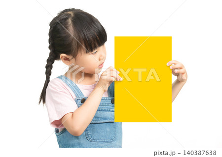 Asian Little Girl with Braided Hair Looking at Yellow Paper Card on White Background Asian Little Girl with Braided Hair Looking at Yellow Paper Card on White Background 140387638