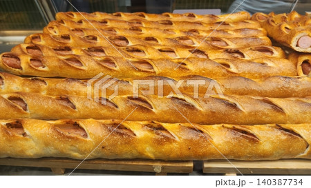 Freshly Baked Long Sausage Bread Rolls with Golden Crust Displayed in a Bakery Shelf 140387734