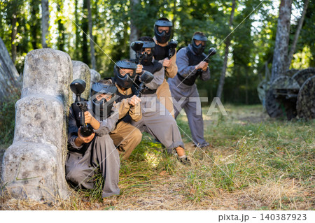 Group of paintball players aiming and shooting with guns outdoors Group of paintball players aiming and shooting with guns outdoors 140387923