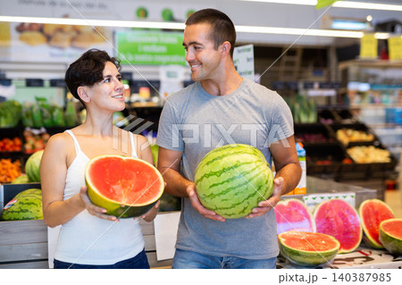 Husband with wife chooses ripe watermelon in supermarket 140387985