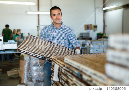 Portrait of male farm worker loading boxes with vegetable seeds in stack on greenhouse plantation 140388006