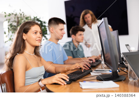 Girl student of computer courses looks at monitor screen, types on keyboard and does work 140388364