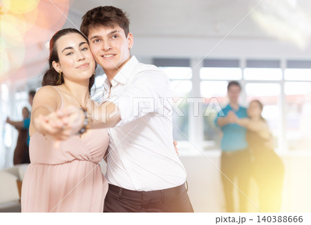 Guy and girl in couple spins to rhythm of tango during lesson for novice students. Classes in mini groups for those who want to learn dancing Guy and girl in couple spins to rhythm of tango during lesson for novice students. Classes in mini groups for those who want to learn dancing 140388666