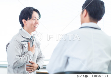 医師の診察を受ける作業着の男性 産業医の面談 健康診断 腹痛 頭痛 相談 医師の診察を受ける作業着の男性 産業医の面談 健康診断 腹痛 頭痛 相談 140389071