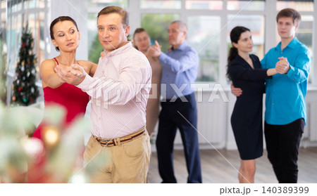 Couples dancing during Christmas - men and women dancing tango or samba next to Christmas tree Couples dancing during Christmas - men and women dancing tango or samba next to Christmas tree 140389399