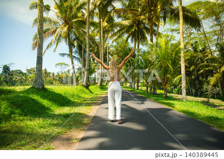 A person joyfully walks along a path of palm trees 140389445