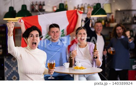 Company of emotional adult young sports fans holding flag of Peru, rejoicing winning match game and drinking beer in bar 140389924
