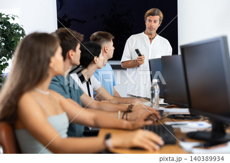 Students of computer courses sit in class near PC, watch to teacher and listen to lecturer Students of computer courses sit in class near PC, watch to teacher and listen to lecturer 140389934