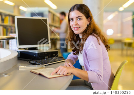 Student girl is working with a book while sitting in front of a computer Student girl is working with a book while sitting in front of a computer 140390256