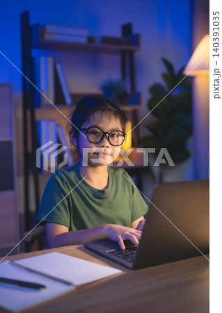 Child Girl Wearing Glasses Sitting at Desk with Laptop in Cozy Home Office During Evening Studying or Working with Books and Notebook Child Girl Wearing Glasses Sitting at Desk with Laptop in Cozy Home Office During Evening Studying or Working with Books and Notebook 140391035